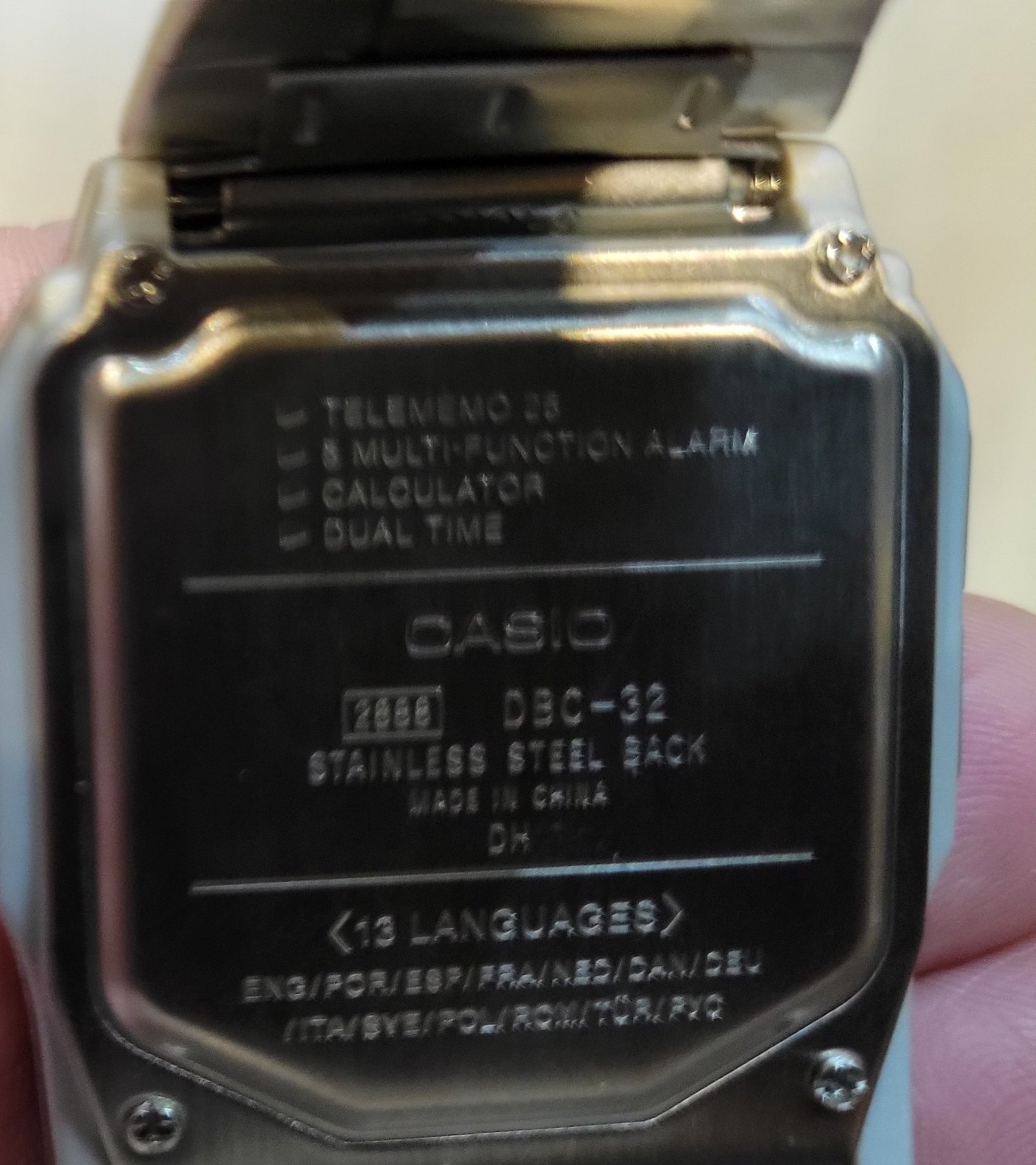 Figure 2 — The back of my DBC-32, photographed whole: the stainless plate with its four screws, and the engraving with module 2888 and the thirteen languages.
