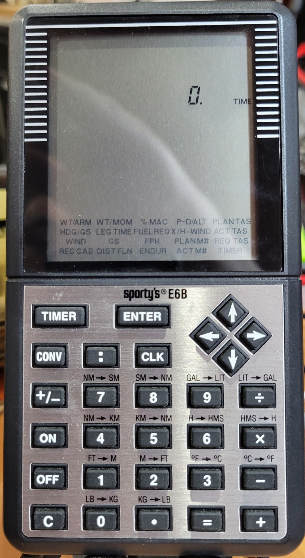 Figure 1 — My Sporty's E6B: the liquid-crystal display with its menu of twenty functions printed along the bottom, the TIMER, ENTER and CONV keys, the arrow pad, and the conversions printed above the number k…