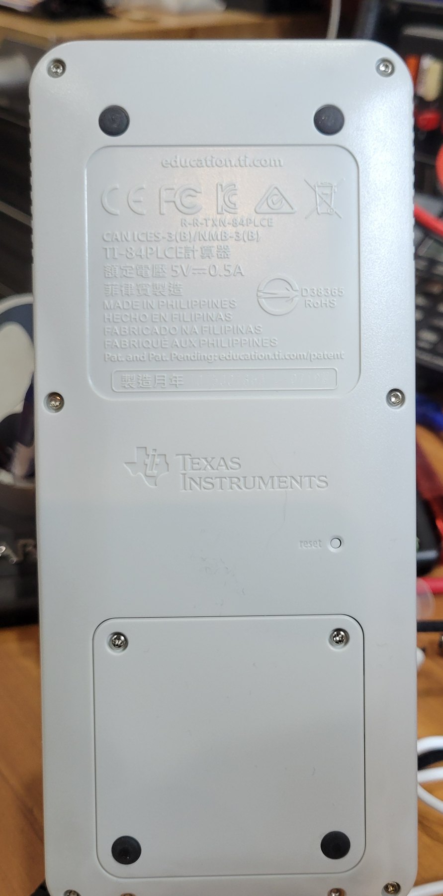 Figure 3 — The back of my TI-84 Plus CE: the moulded label, the reset hole to the right of the TI logo, and the screwed cover over the battery.