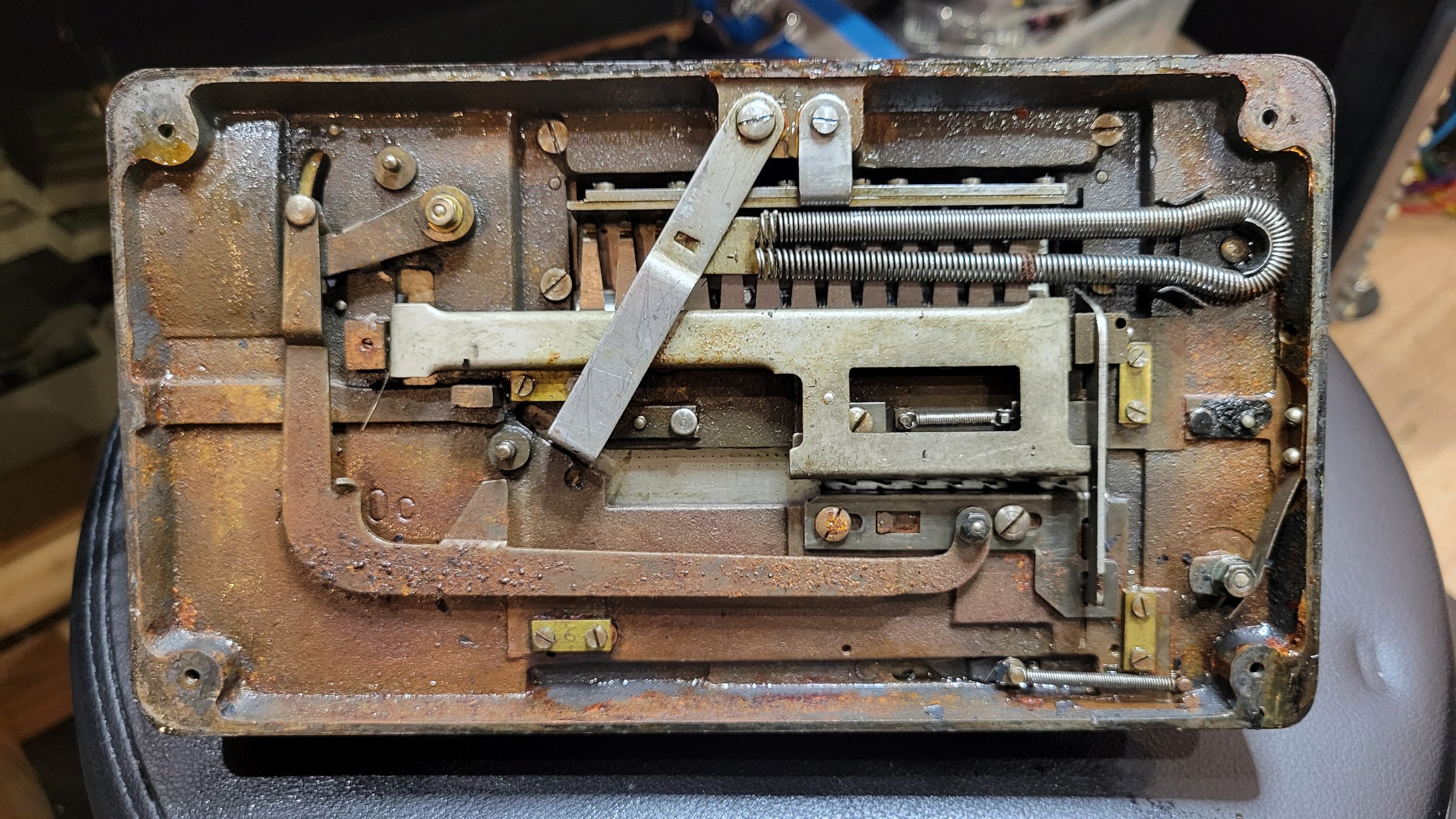 Figure 4 — The underside of my Manus with the bottom pan removed: the carriage-control linkage, the long double carriage spring at the top right, the division rack with its small spring in the window, and the…
