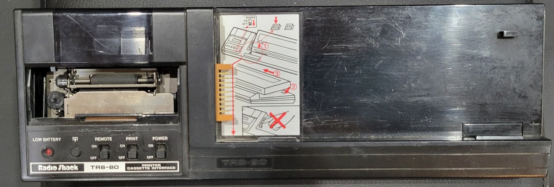 Figure 1 — My 26-3505 Printer/Cassette Interface with the computer removed: the printer at the left under its clear paper cover, the switches and LOW BATTERY lamp below it, the connector in the cradle, and th…