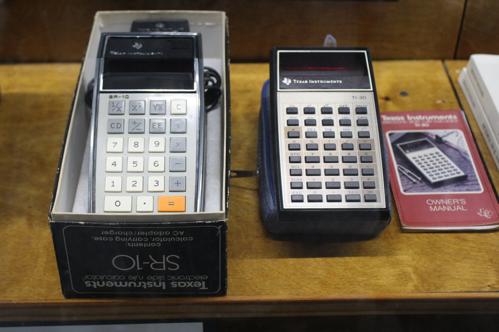 Figure 10 — A TI SR-10 in its box beside a TI-30 and its owner's manual, at the Tallahassee Automobile Museum.